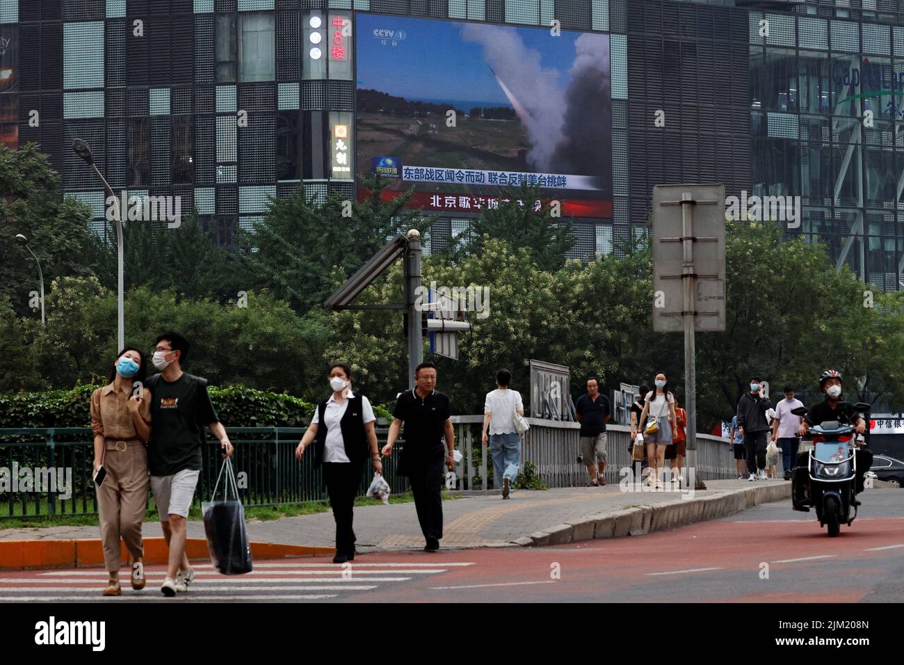 Pedestrians walk past a giant screen broadcasting news report on Chinese People's Liberation Army's (PLA) military exercises around Taiwan, in Beijing, China August 4, 2022. REUTERS/Thomas Peter Stock Photo
