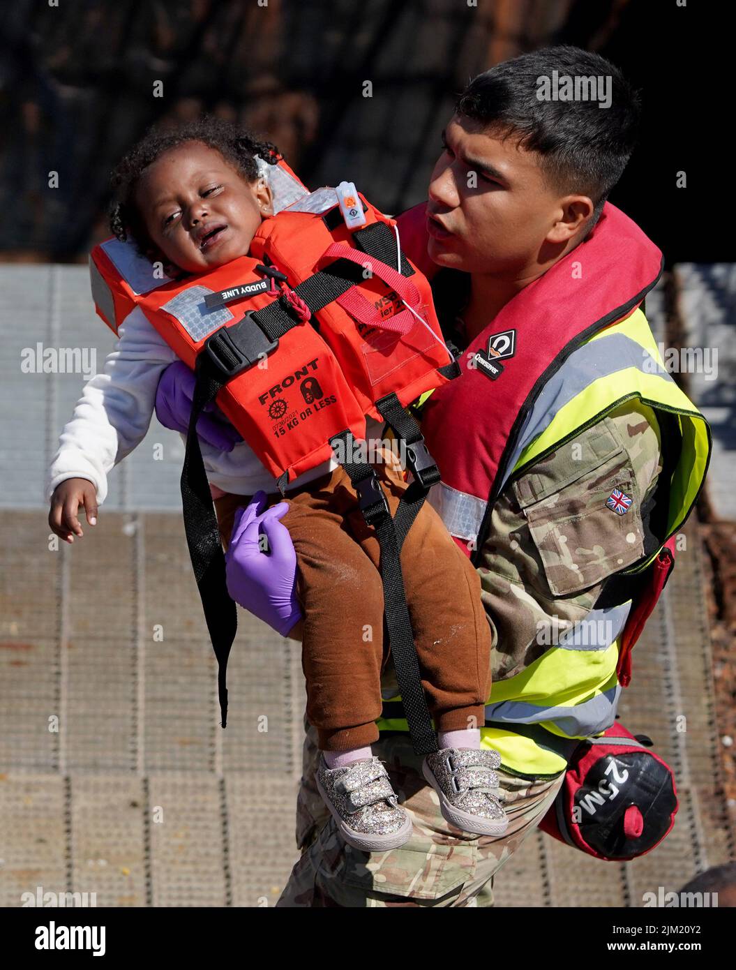 EDITORS NOTE: The PA Picture Desk has been unable to gain the necessary permission to photograph children under 16 on issues involving their welfare. This image has been provided unpixelated for customers to pixelate in their own style. A distressed young girl is carried by a military officer as group of people thought to be migrants are brought in to Dover, Kent, following a small boat incident in the Channel. Picture date: Thursday August 4, 2022. Stock Photo