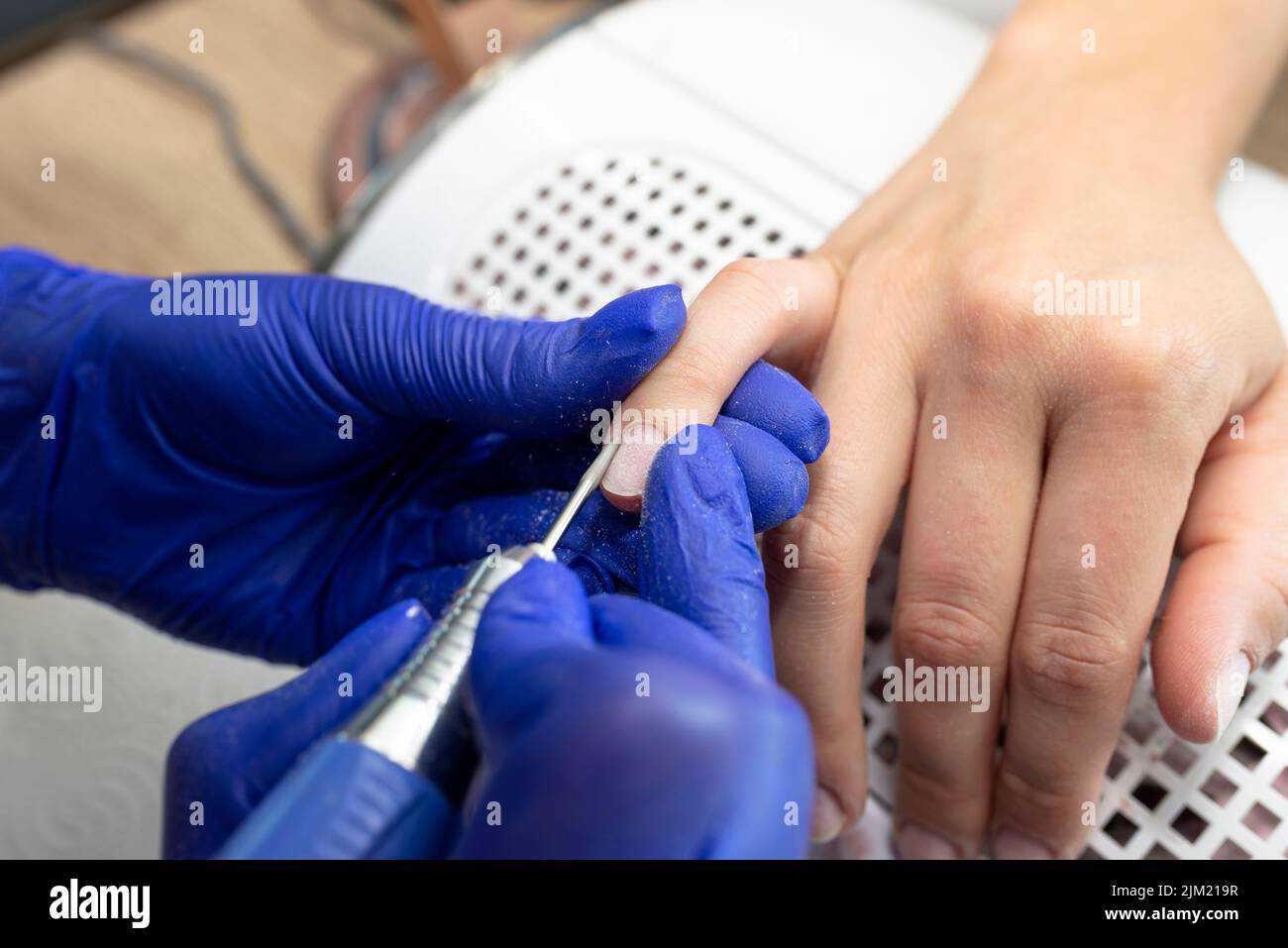 The manicurist cuts the cuticles of the nails with an electric milling machine wearing blue latex gloves. Stock Photo