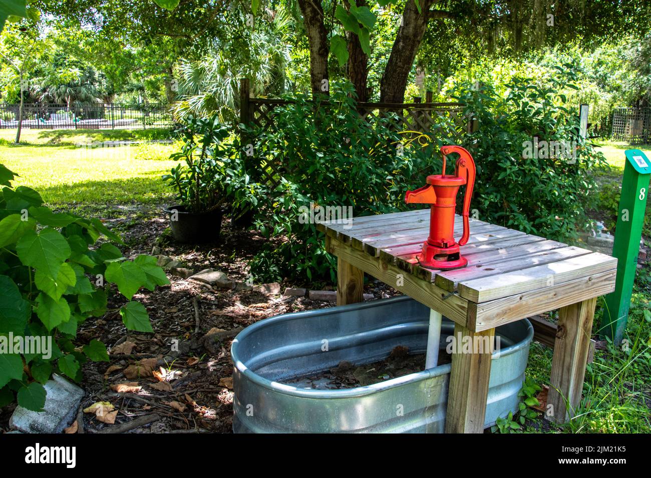Antique vintage red water pump on a wooden table over a silver metal trough in a garden. Garden design: Punta Gorda, Florida, History Park, Charlotte Stock Photo
