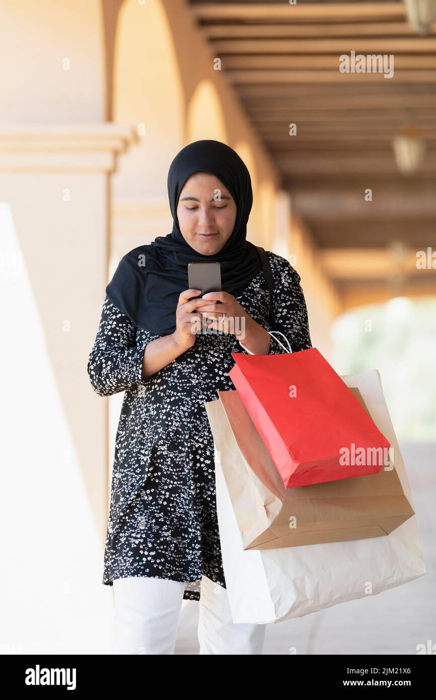 Muslim woman carrying shopping bags checking her phone Stock Photo