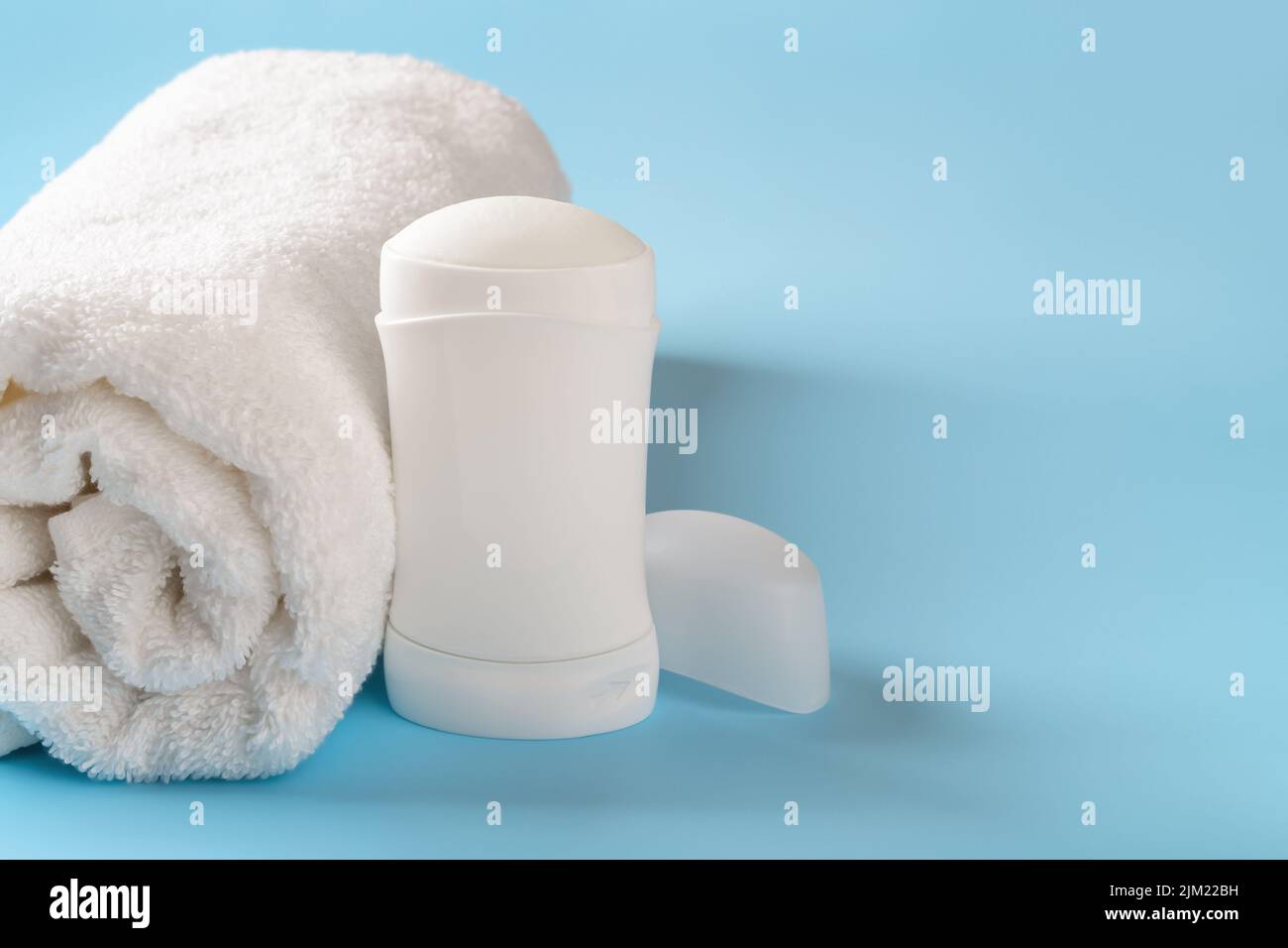 Solid antiperspirant deodorant and rolled bath towel on a blue background. Personal hygiene items, body care, toiletries concepts. Cosmetics, purity. Stock Photo