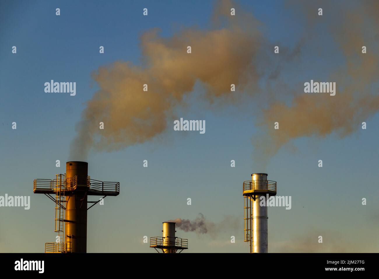 Goiania, Goiás, Brazil – August 04, 2022: Smoke coming out of three chimneys of a factory. Air pollution by smoke coming out of the chimney. Stock Photo