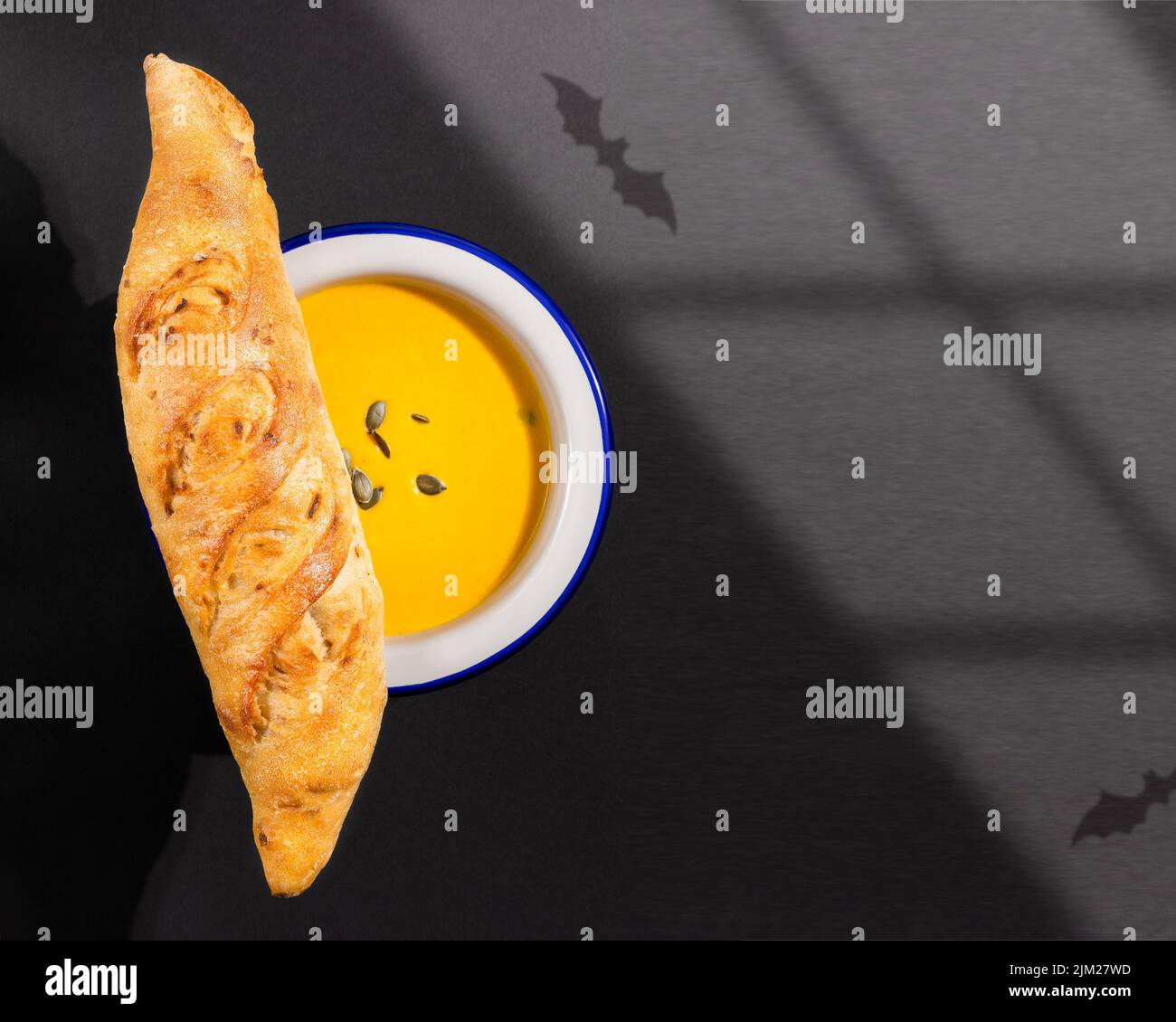 Halloween, food composition with home made pumpkin soup puree with fresh crunchy french baguette on a black background with bats shadows. Mystical, ha Stock Photo