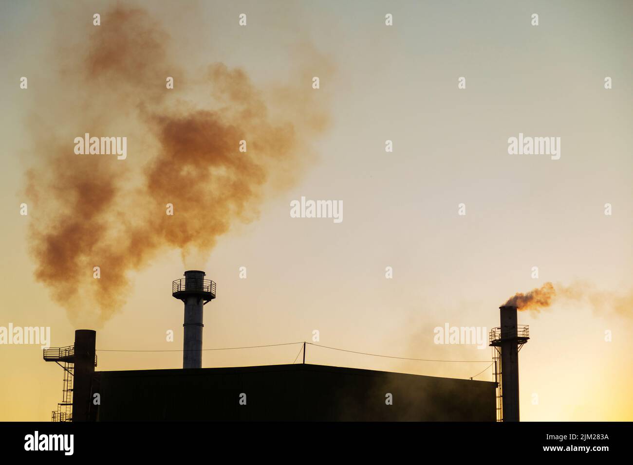 Goiania, Goiás, Brazil – August 04, 2022: Smoke coming out of three chimneys of a factory. Air pollution by smoke coming out of the chimney. Stock Photo