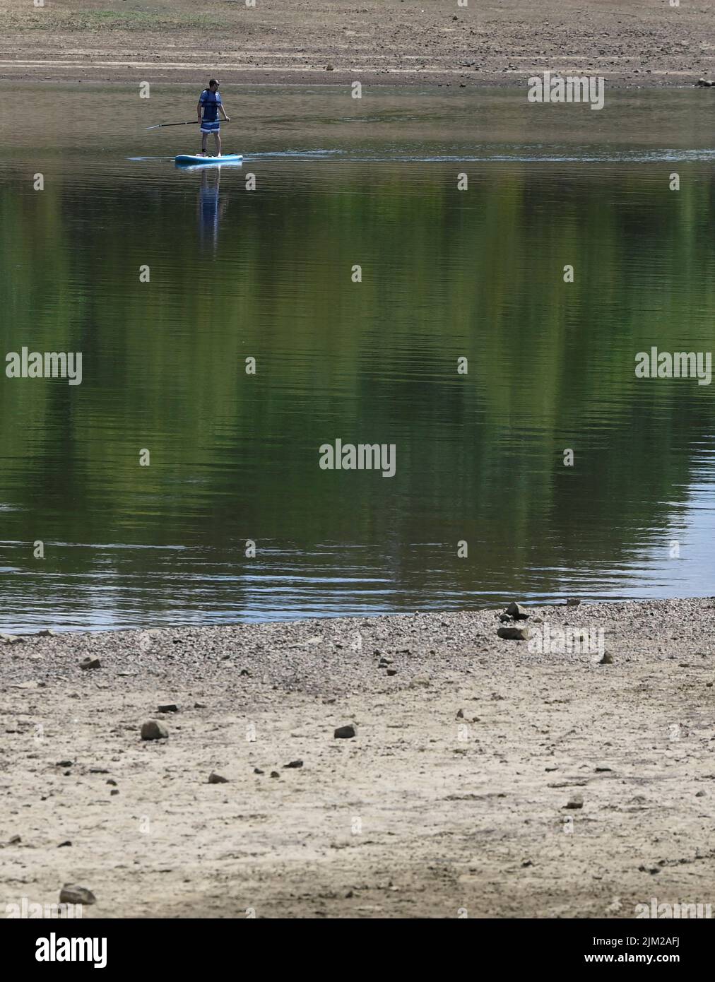 A man uses a paddle board as reduced water levels are seen at Ardingly Reservoir, ahead of regional restrictions over water usage being implemented in the hot and dry weather, Ardingly, southern Britain, August 4, 2022.  REUTERS/Toby Melville Stock Photo
