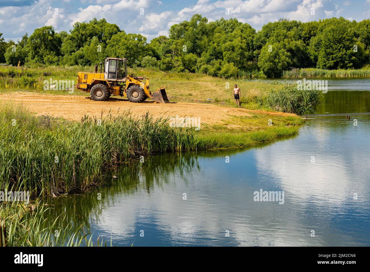 tractor rakes sand on the river beach in summer Stock Photo