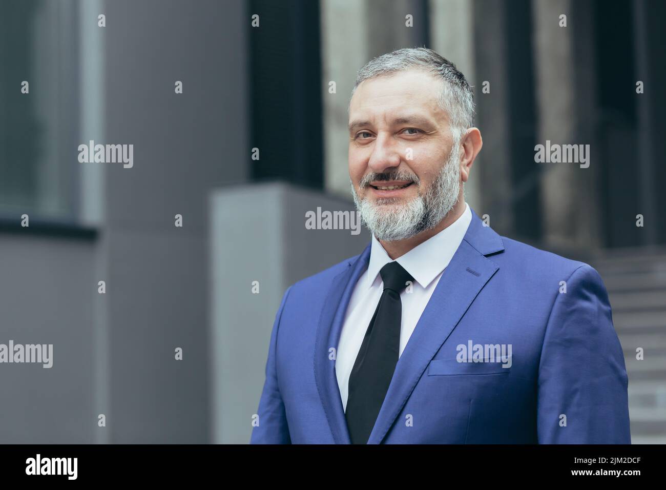 Close up photo portrait of successful and senior experienced businessman, boss smiling and looking at camera, man in business suit standing outside office building Stock Photo