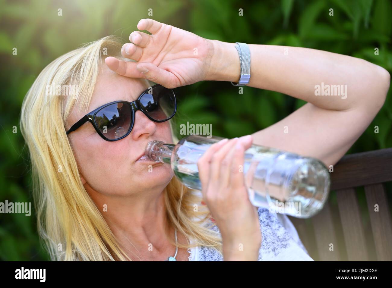 Woman Drinks Water In The Garden, Heat Wave Stock Photo