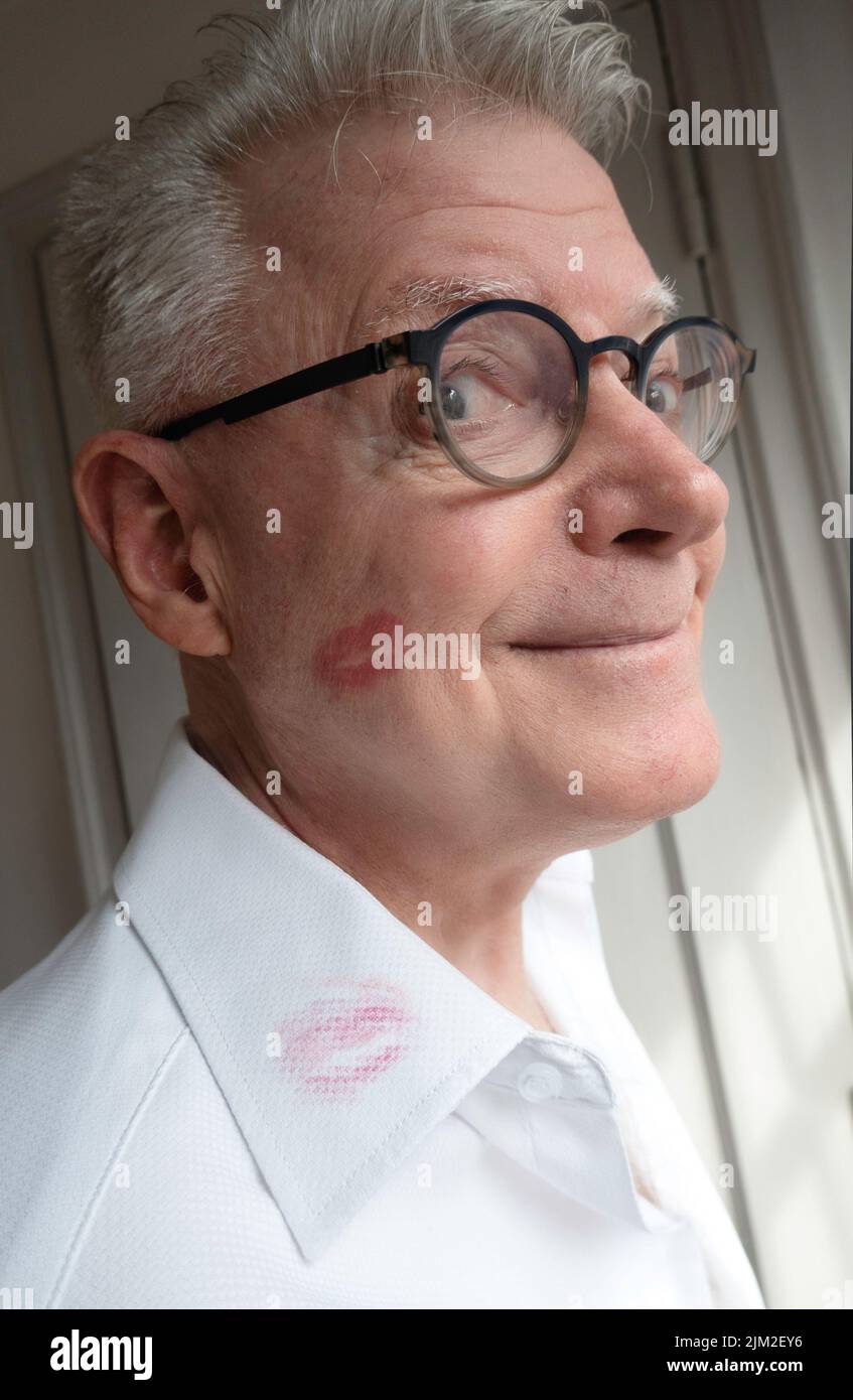 Senior man smirks showing off a lipstick smudge on his white shirt collar Stock Photo