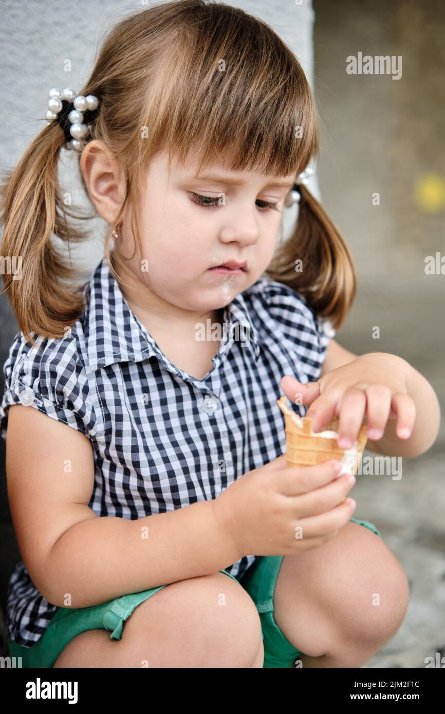 Little baby girl eating ice cream, licking her fingers. Cute kid