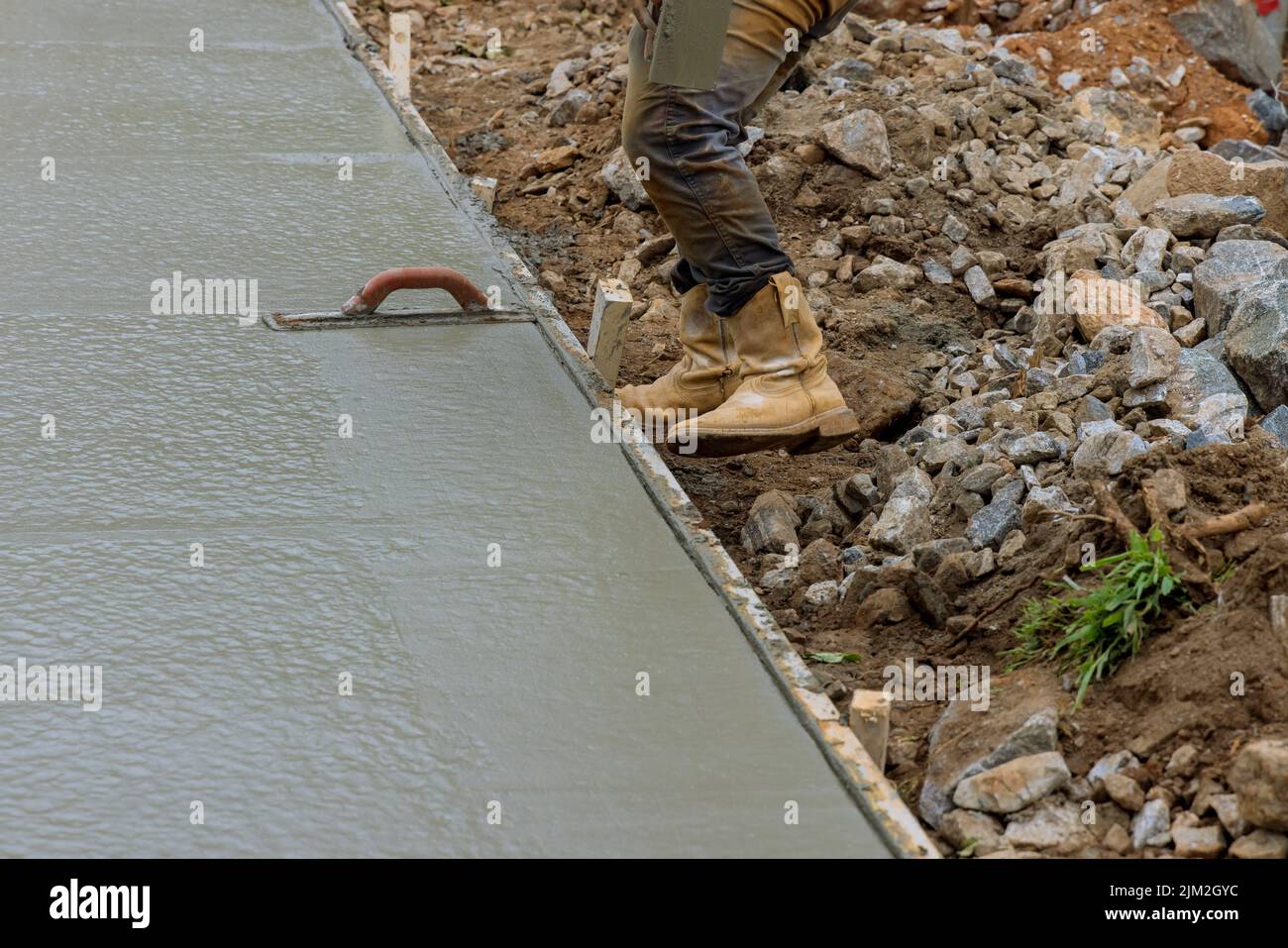 Worker is holding a steel trowel and smoothing plastering over freshly poured concrete that is wet Stock Photo