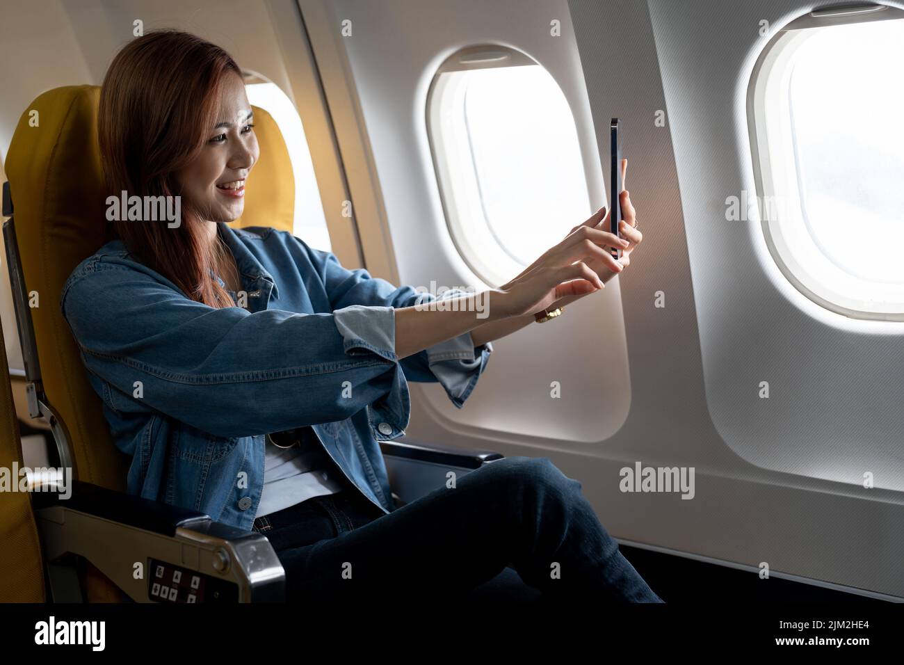 Beautiful Asian woman take a selfie with mobile phone in airplane Stock Photo