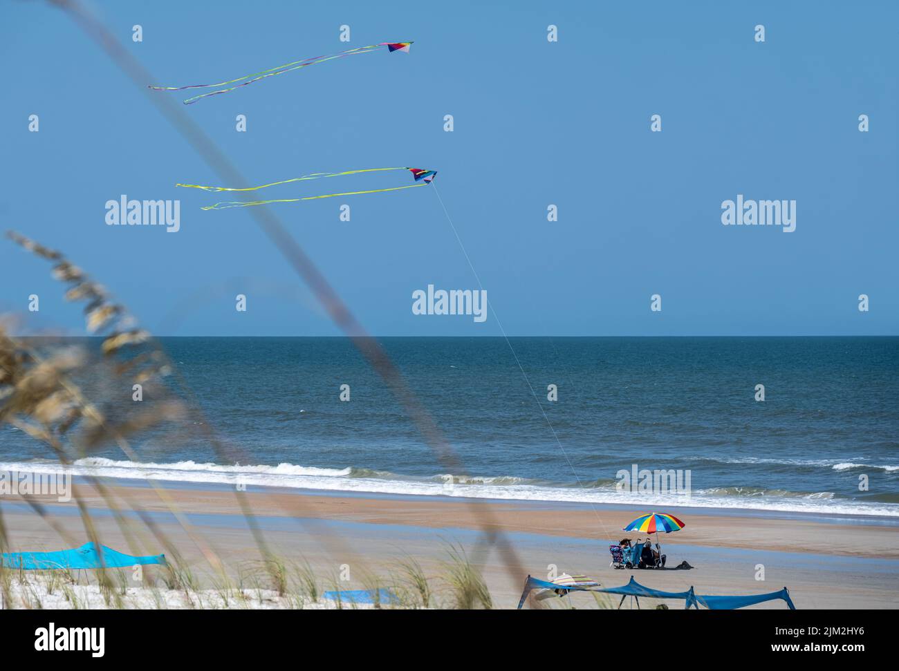 Senior couple enjoying a beautiful day at the beach in St. Augustine, Florida, shaded by a colorful beach umbrella while kites fly overhead. (USA) Stock Photo