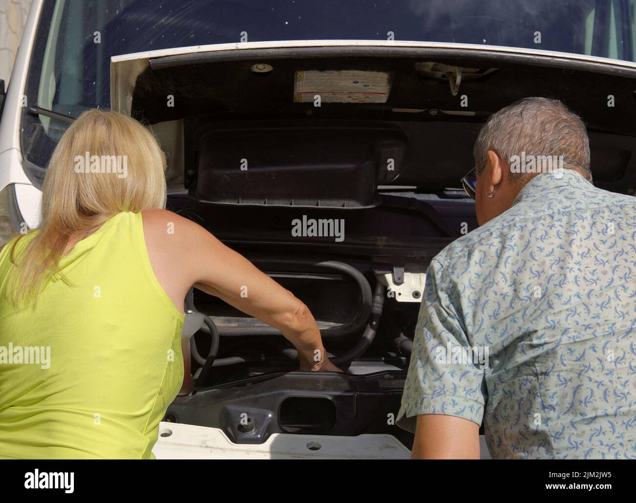 A couple looks at the engine inside the hood of the car Stock Photo Alamy