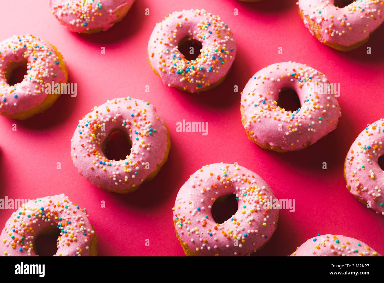 High angle view of fresh pink donuts with sprinklers against colored background Stock Photo
