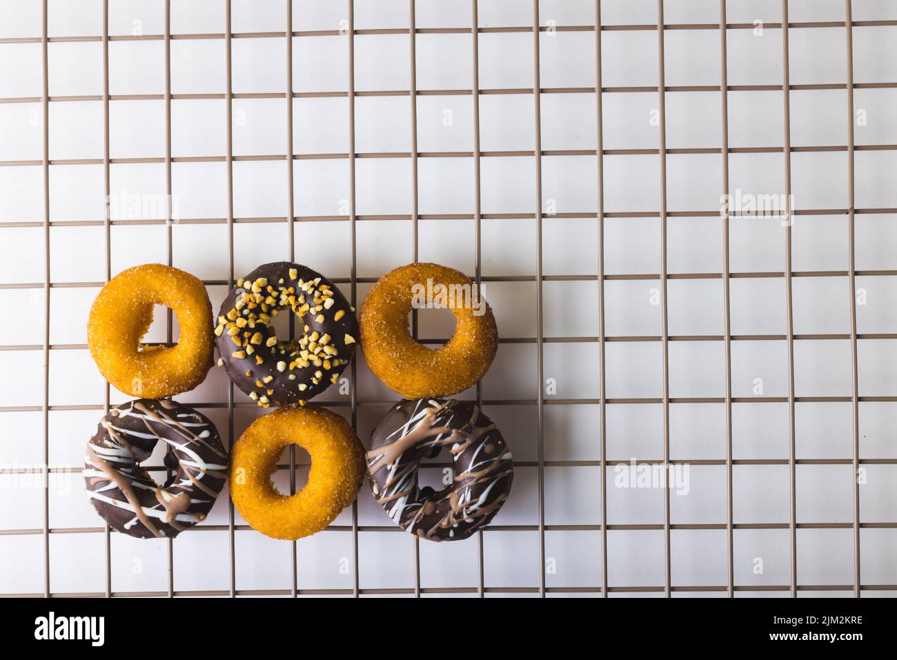 Directly above view of various fresh donuts on cooling rack over white background. unaltered, unhealthy eating and sweet food concept. Stock Photo