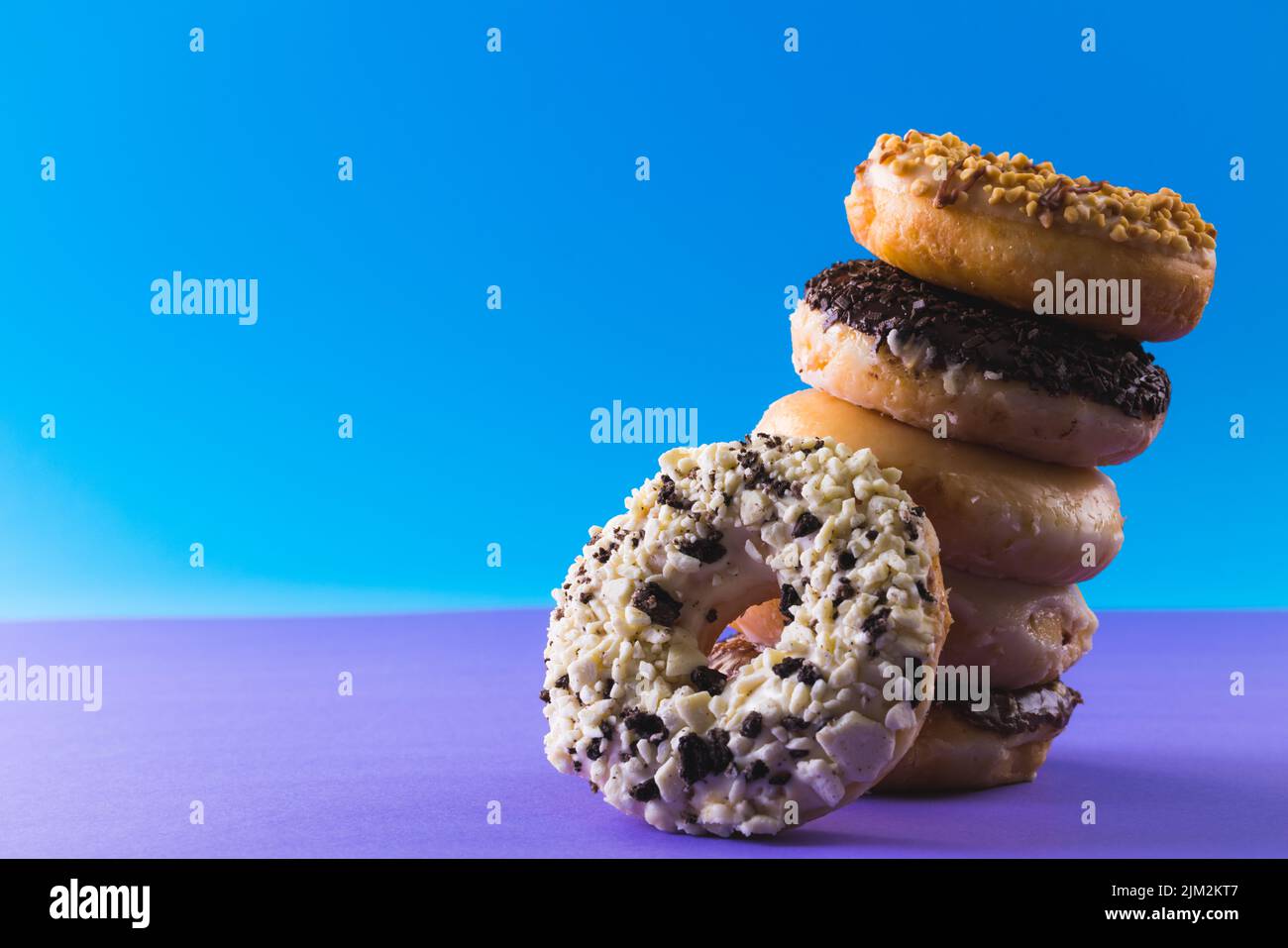 Close-up of fresh donuts stacked tilted by copy space against blue background. unaltered, unhealthy eating and sweet food concept. Stock Photo