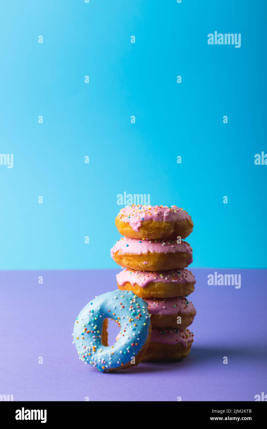 Fresh donuts with sprinklers stacked against blue background with copy