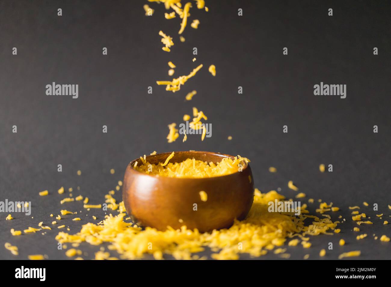 Grated yellow cheese and bowl against gray background, copy space. unaltered, food, motion, studio shot and dairy product. Stock Photo