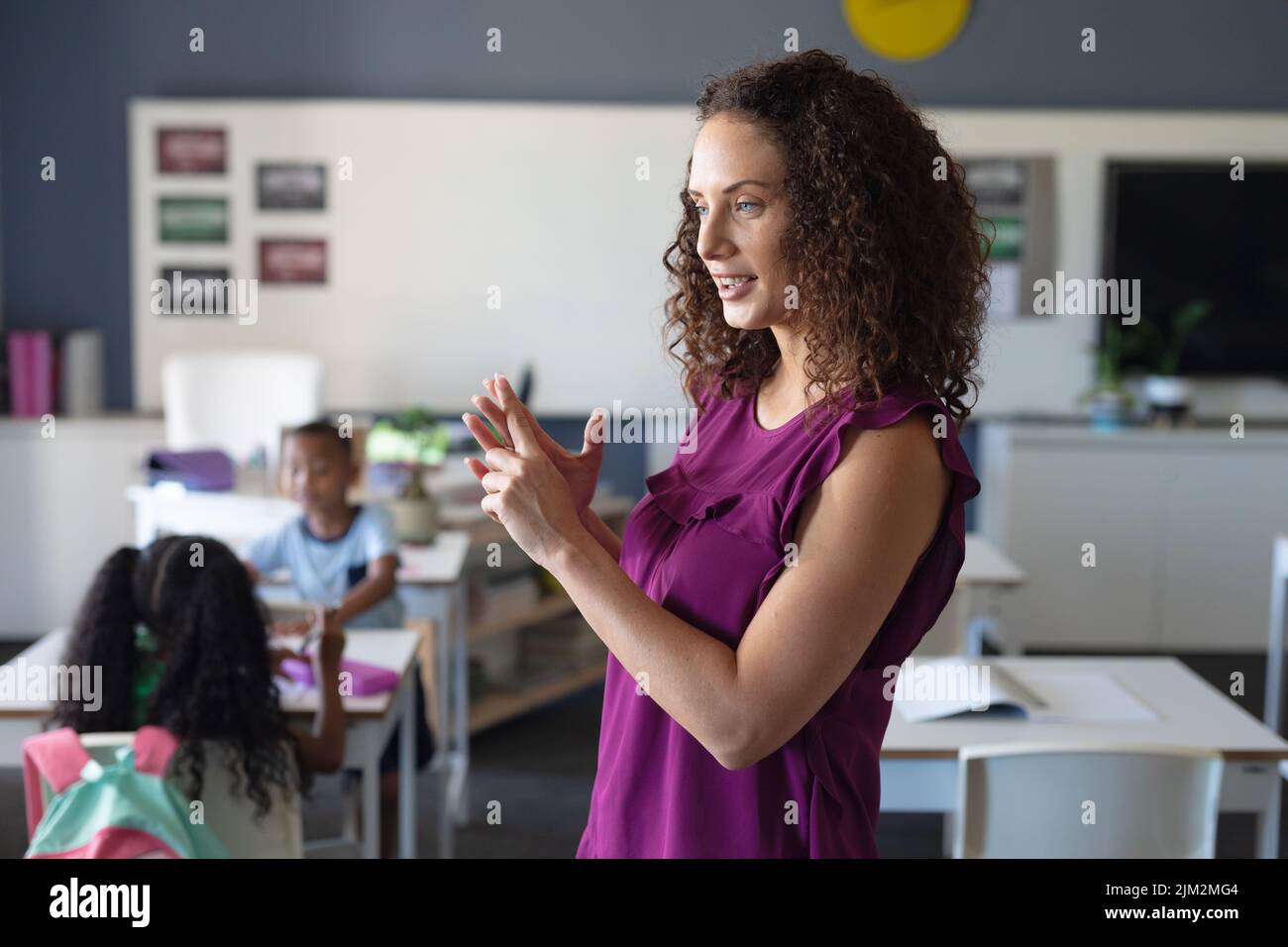 Caucasian young female teacher with curly hair gesturing while teaching in classroom Stock Photo