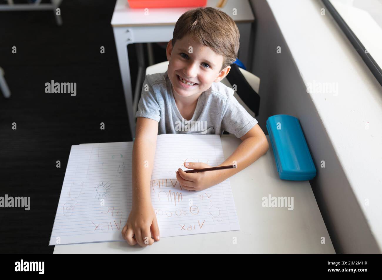 High angle portrait of smiling caucasian elementary schoolboy with book and pen sitting at desk. unaltered, education, childhood, learning and school Stock Photo