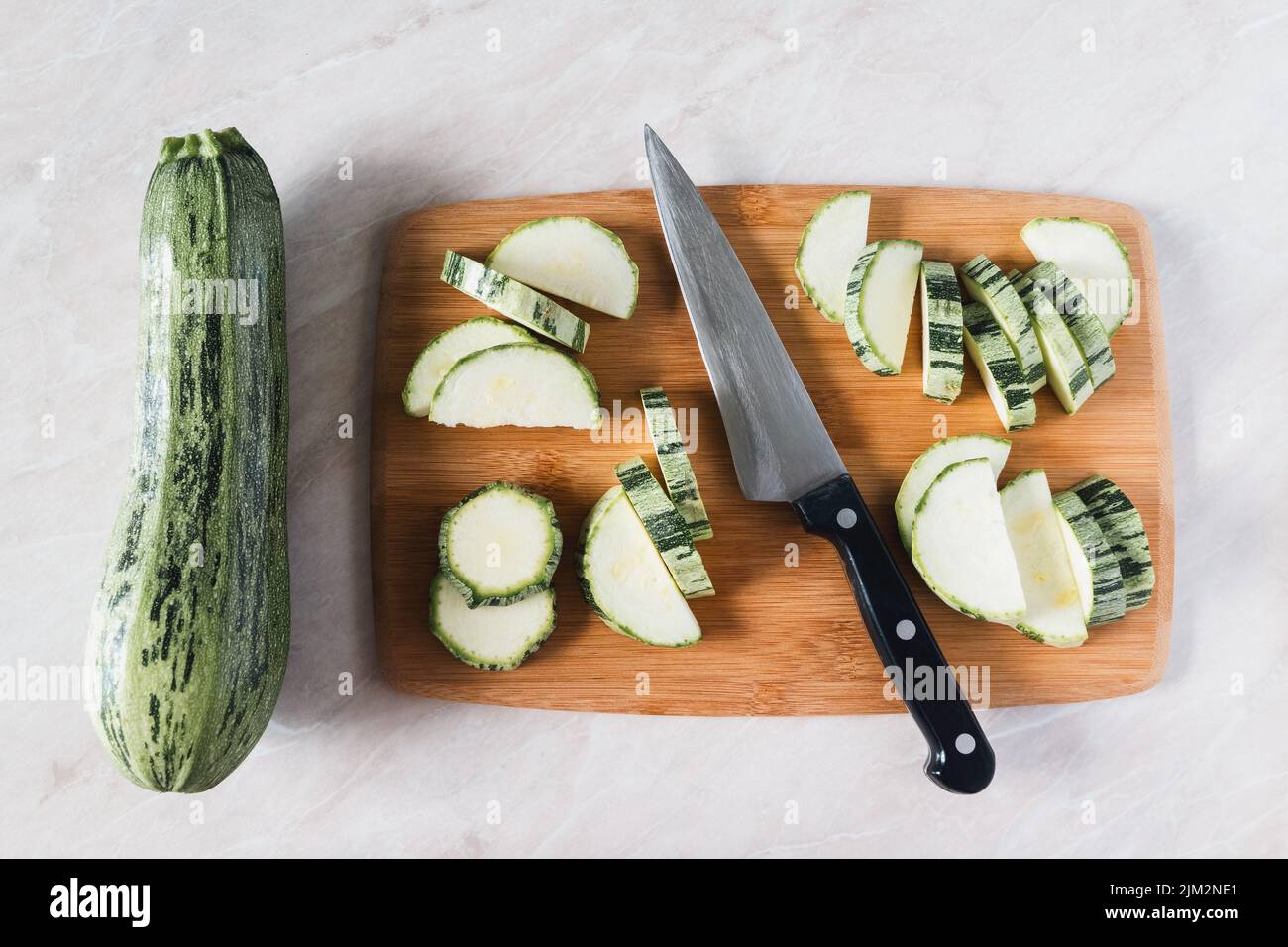 Cutting zucchini on wooden board, whole squash, knife and slices