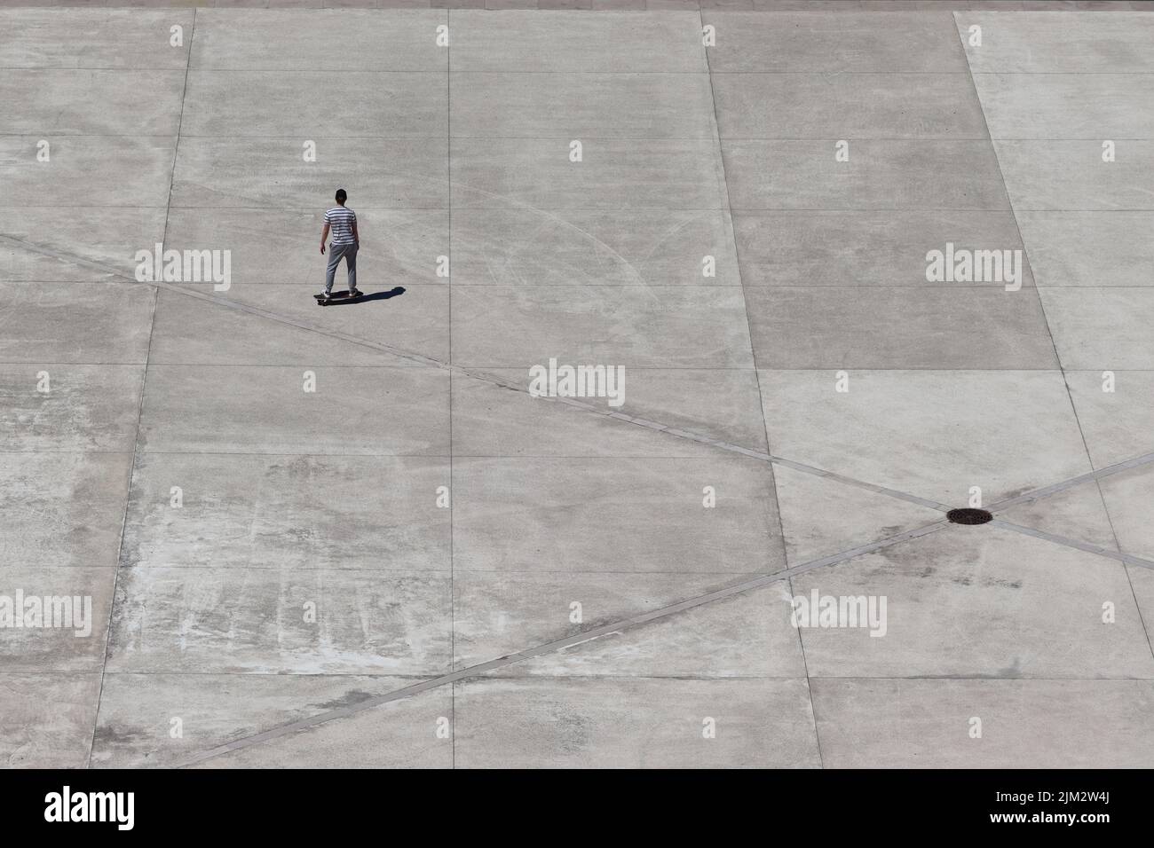 A lone male skateboarder prepares to enjoy the freedom this vast expanse affords on Lisbon seafront. Stock Photo