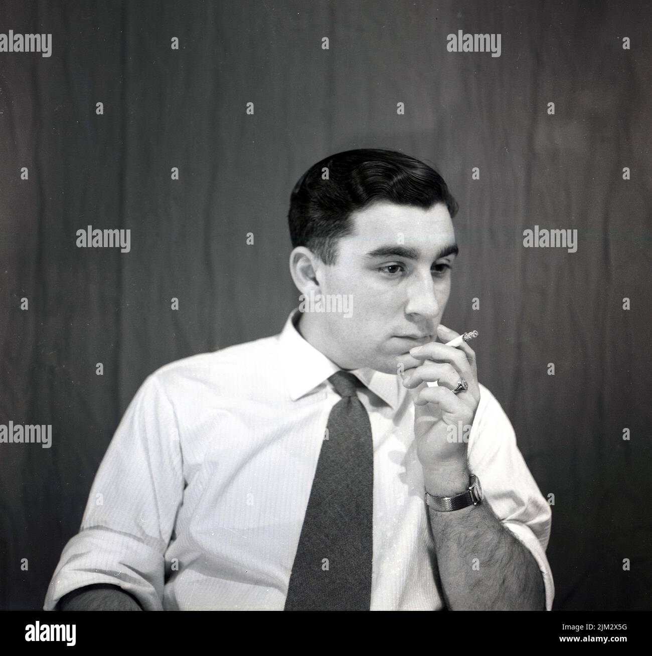 1950s, historical, man  in a shirt & tie sitting, smoking a cigarette, thinking. Stock Photo