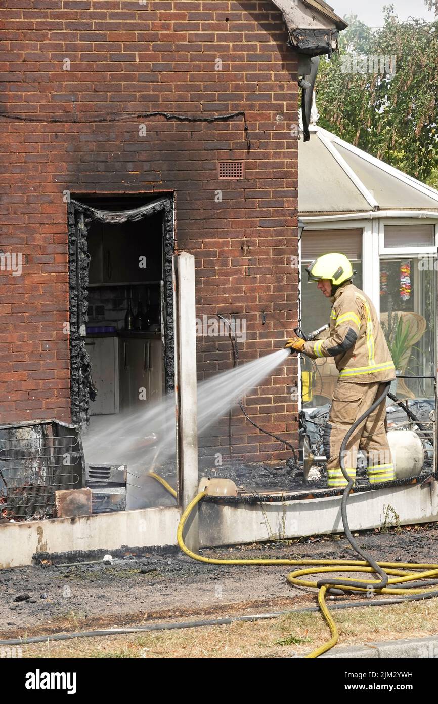 House fire between timber boundary fence & side wall fireman damping down blaze brought under control charred UPVC kitchen door frame Essex England UK Stock Photo