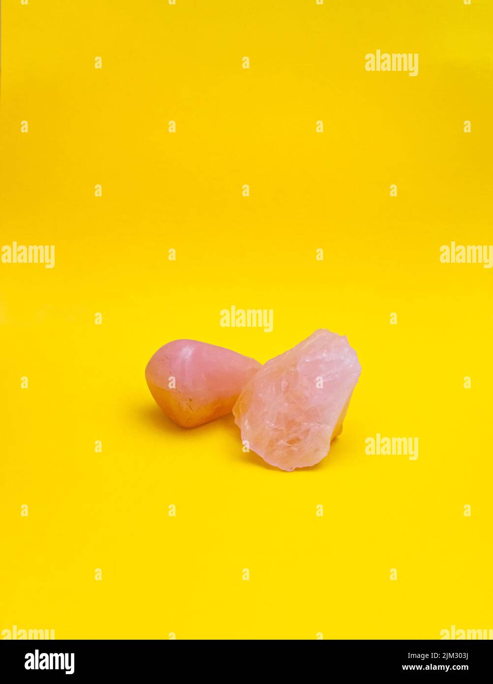 Polished rose quartz and rough/raw rose quartz crystals on a plain, bright yellow background with copy space. Stock Photo