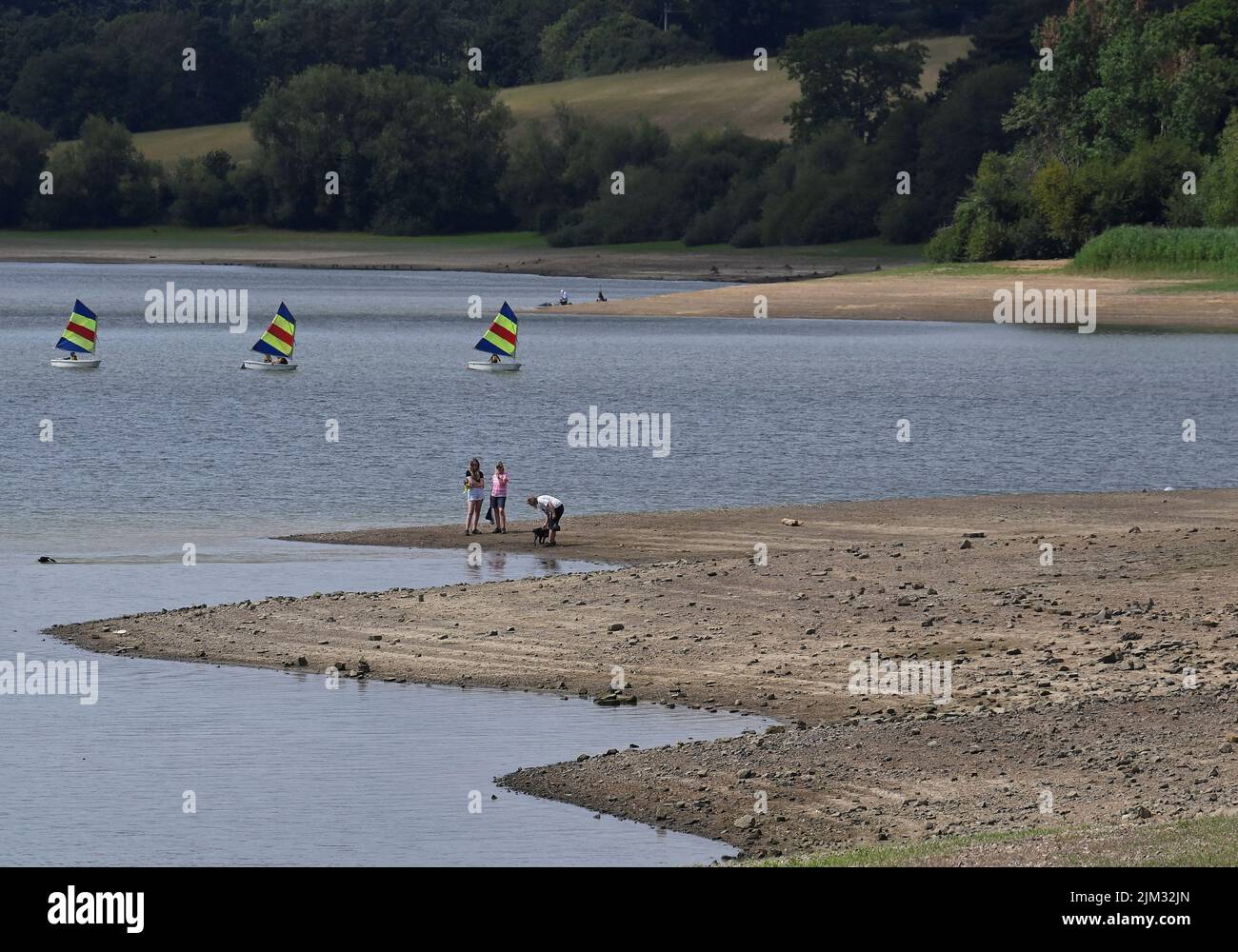 People walk along the shoreline as reduced water levels are seen at Ardingly Reservoir, ahead of regional restrictions over water usage being implemented in the hot and dry weather, Ardingly, southern Britain, August 4, 2022.  REUTERS/Toby Melville Stock Photo
