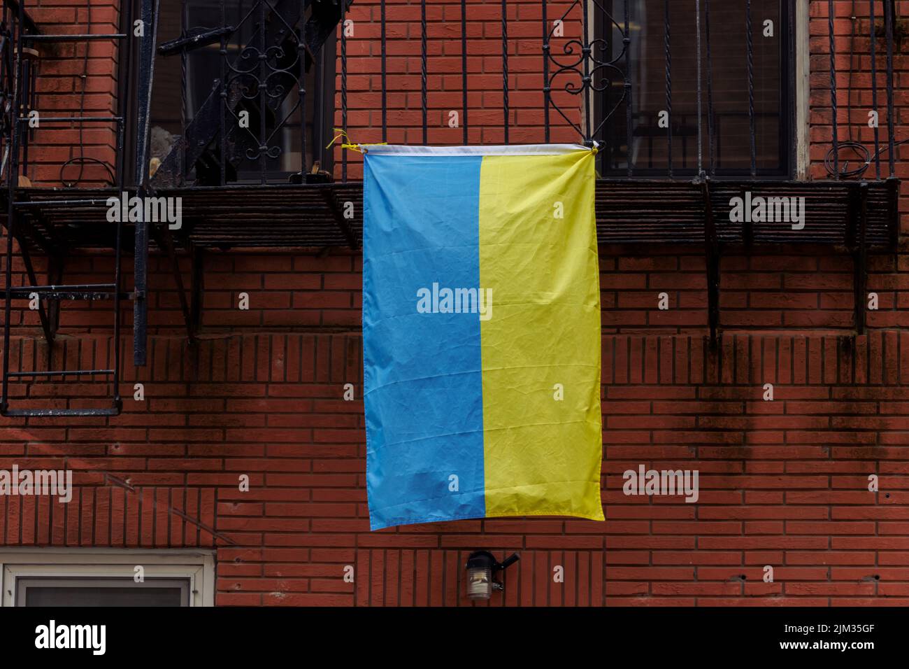 a Ukrainian flag hanging from a fire escape off the side of a red brick building in new york city, showing solidarity with Ukraine Stock Photo