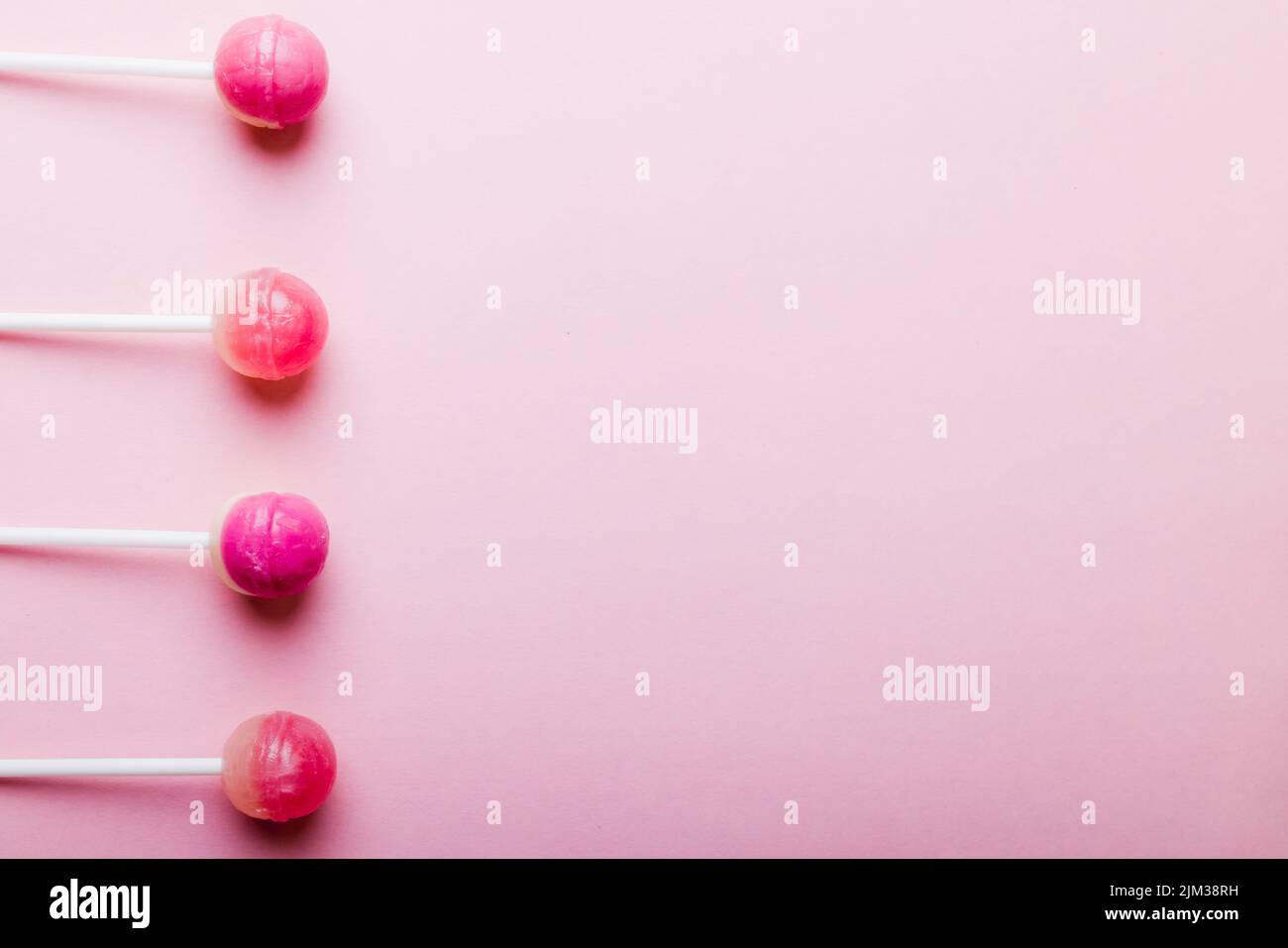 Directly above view of lollipops arranged side by side with copy space over pink background. unaltered, unhealthy eating and sweet food concept. Stock Photo