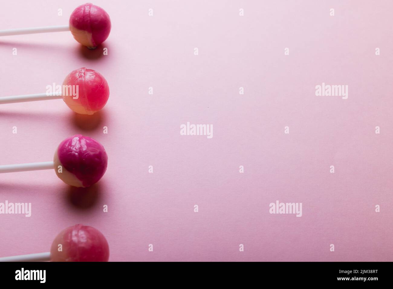 Overhead view of lollipops arranged side by side with copy space against pink background Stock Photo