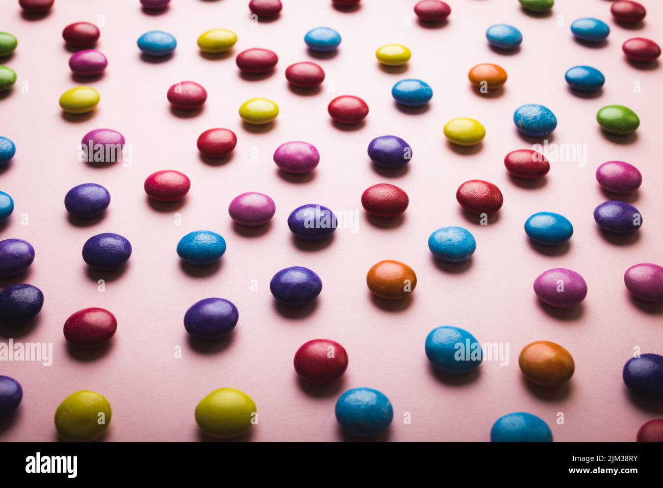 High angle full frame view of multi colored chocolate candies scattered on pink background. unaltered, unhealthy eating and sweet food concept. Stock Photo