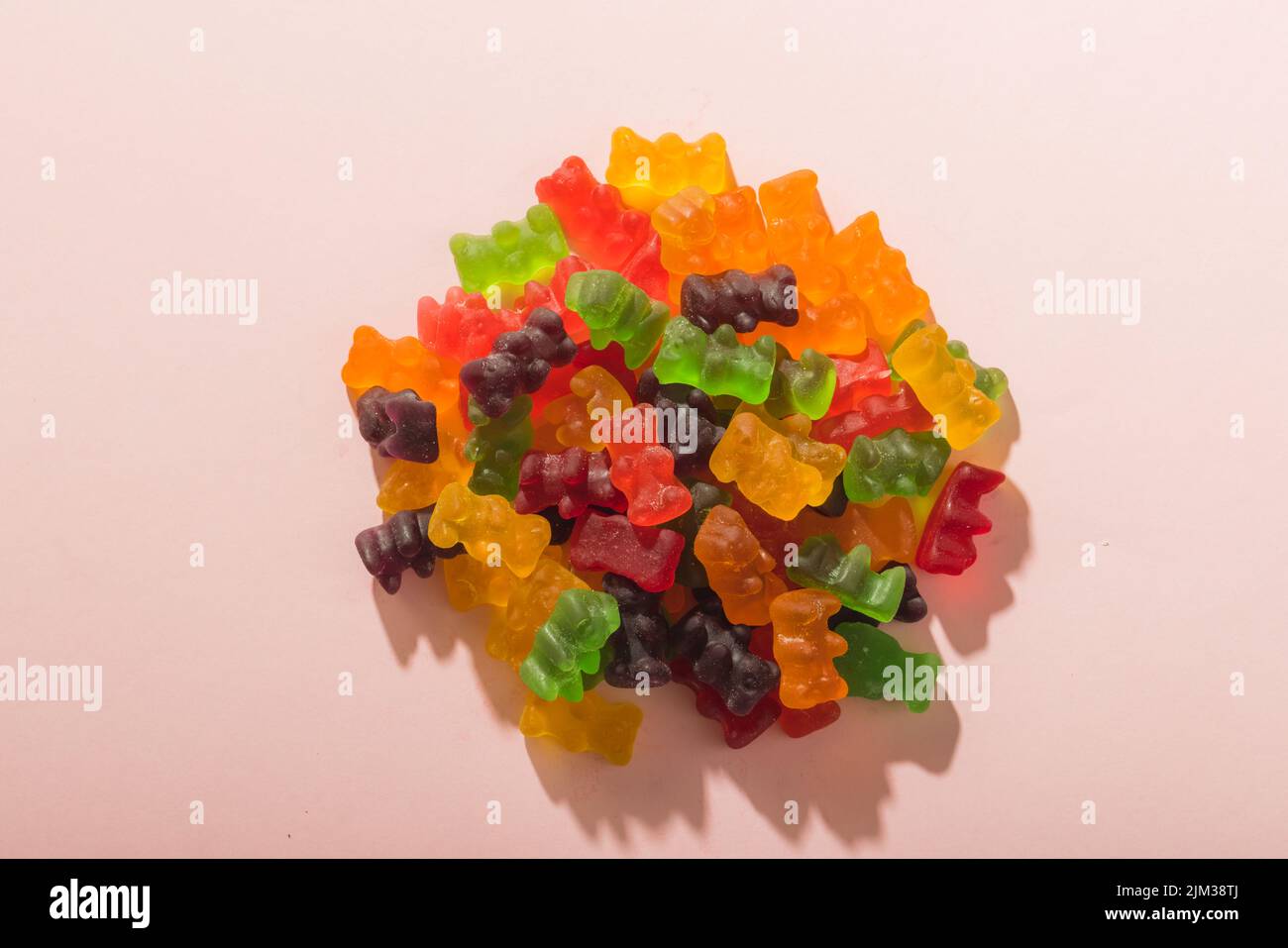 Directly above view of multi colored gummy bears pile amidst copy space on pink background Stock Photo