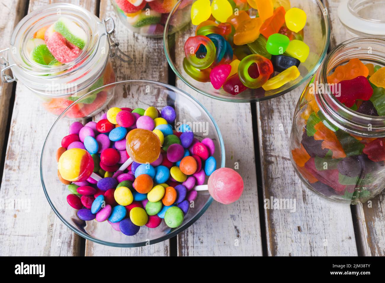 High angle view of multi colored various lollipops and candies in bowls and jars on wooden table. unaltered, unhealthy eating and sweet food concept. Stock Photo