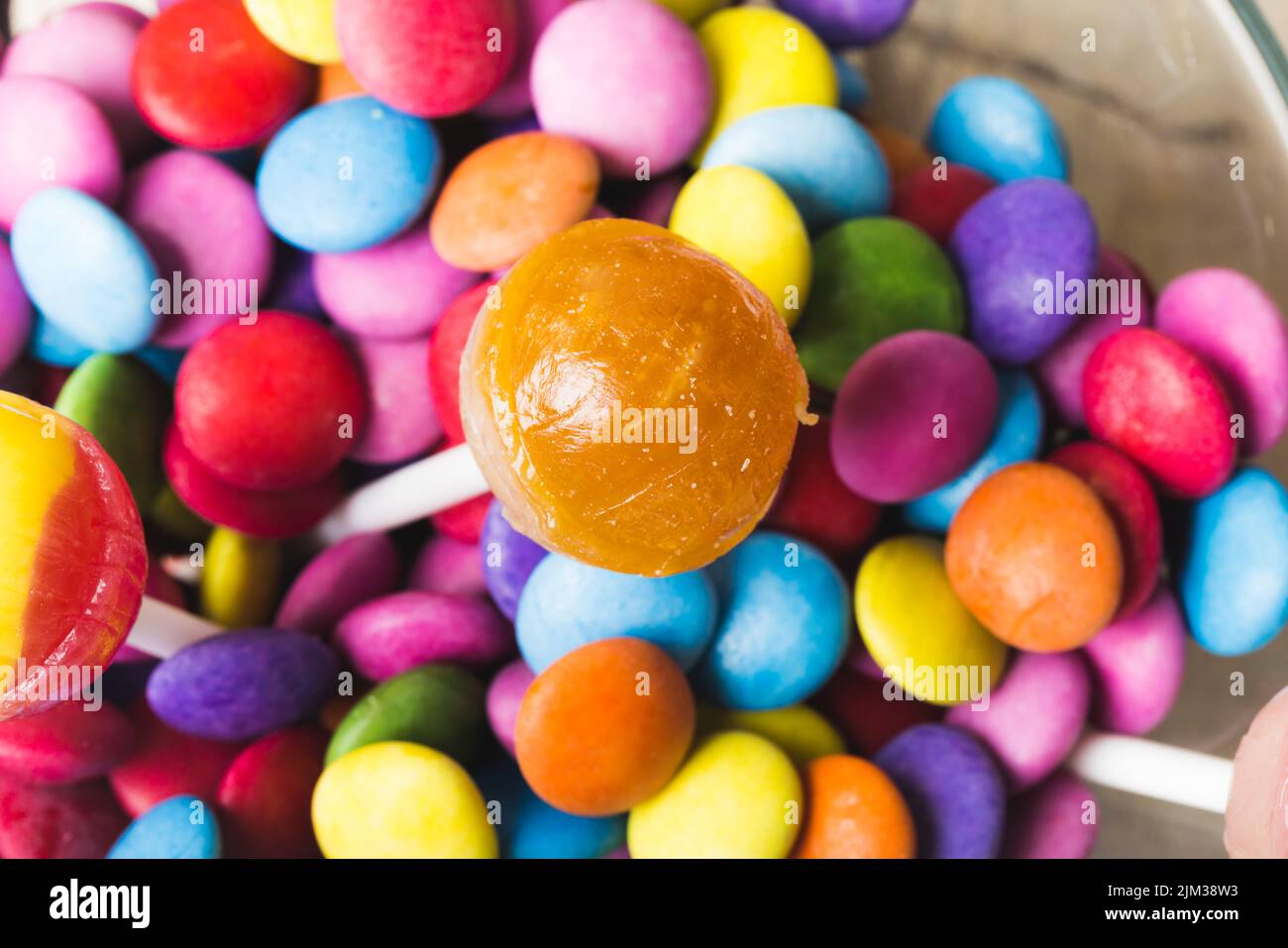 Close-up of lollipop with multi colored chocolate candies in bowl. unaltered, unhealthy eating and sweet food concept. Stock Photo