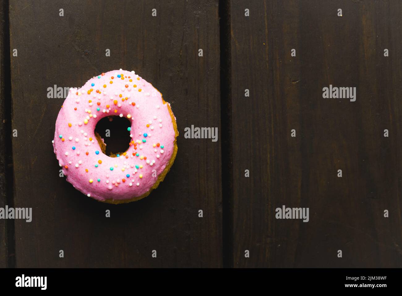 Directly above view of fresh pink donut with sprinklers on wooden table. unaltered, unhealthy eating and sweet food concept. Stock Photo