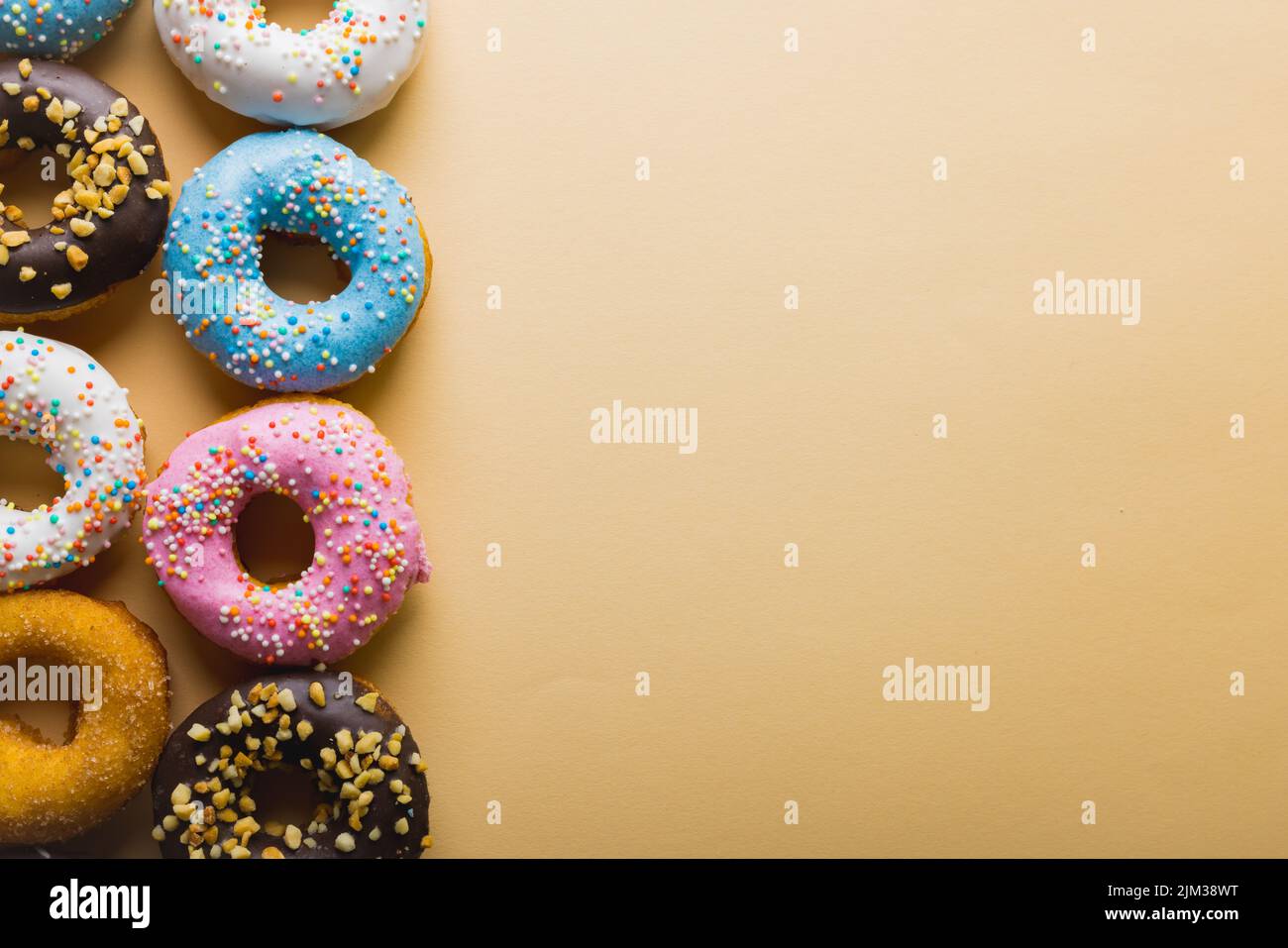 Overhead view of copy space by fresh multi colored donuts arranged on beige background. unaltered, unhealthy eating and sweet food concept. Stock Photo