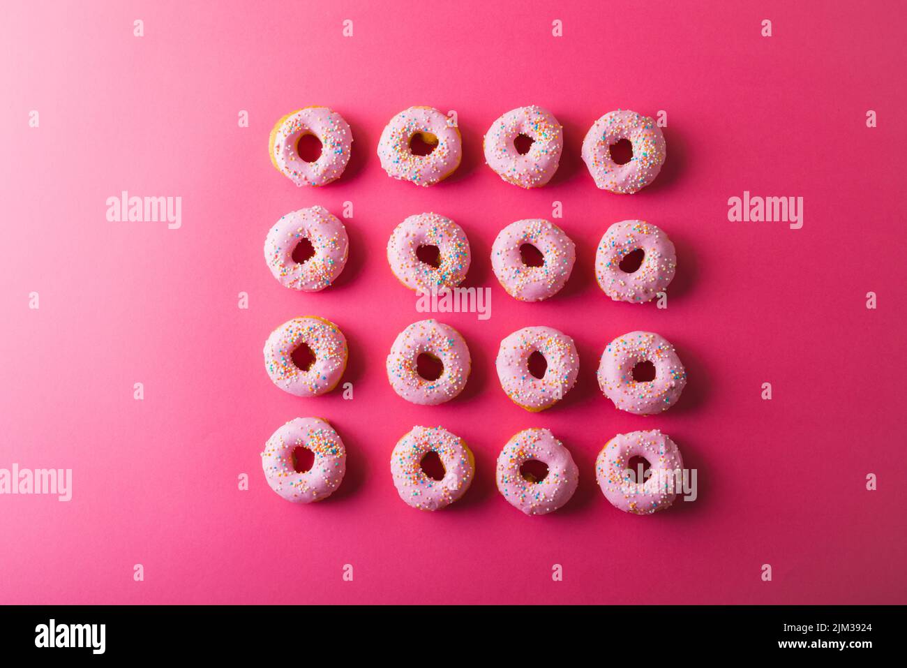Directly above view of fresh donuts with sprinklers arranged by copy space on pink background. unaltered, unhealthy eating and sweet food concept. Stock Photo
