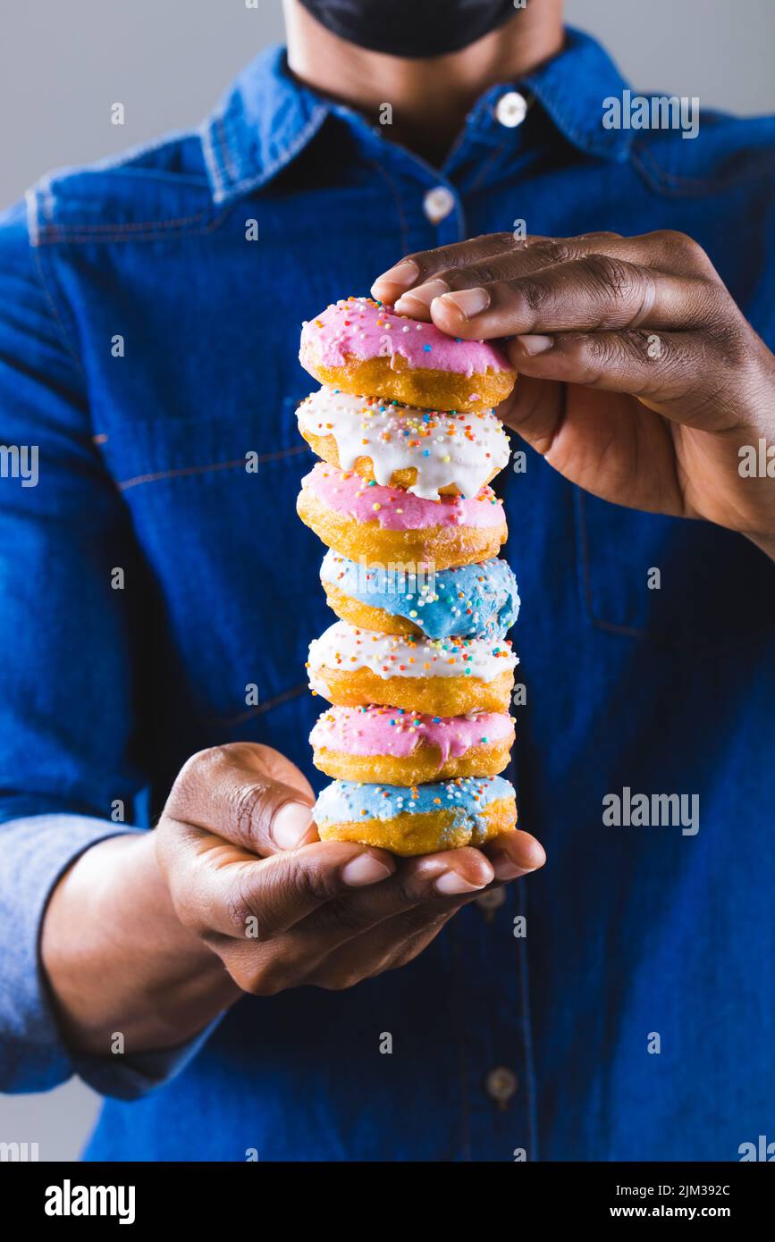 Midsection of african american man holding fresh donuts with sprinklers stack. unaltered, unhealthy eating and sweet food concept. Stock Photo