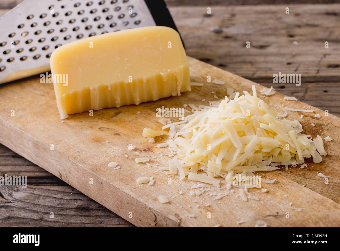 Close-up of grated cheese with grater on wooden board, copy space Stock Photo