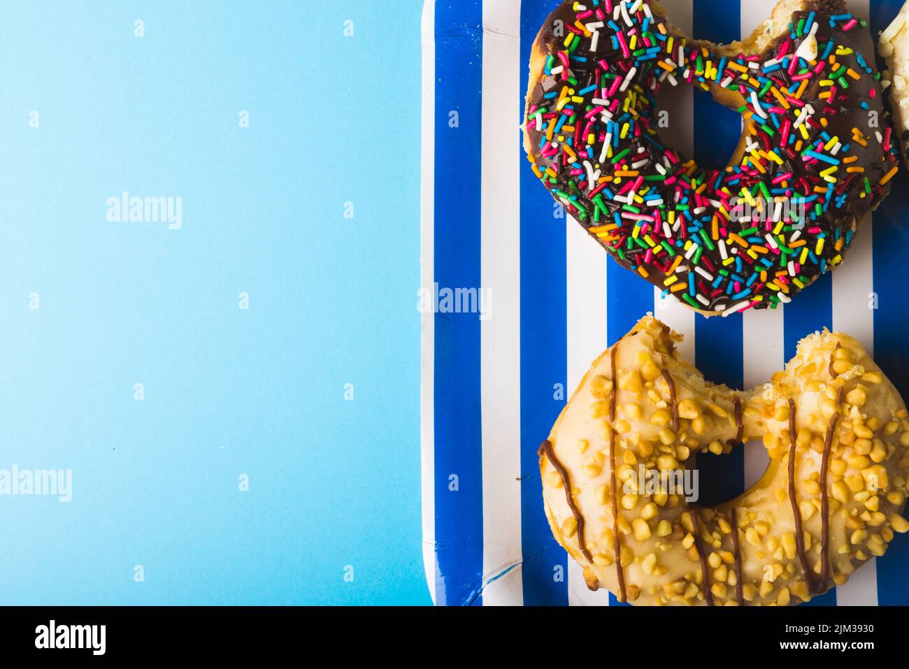 Directly above view of fresh donuts in striped plate by copy space against blue background. unaltered, unhealthy eating and sweet food concept. Stock Photo