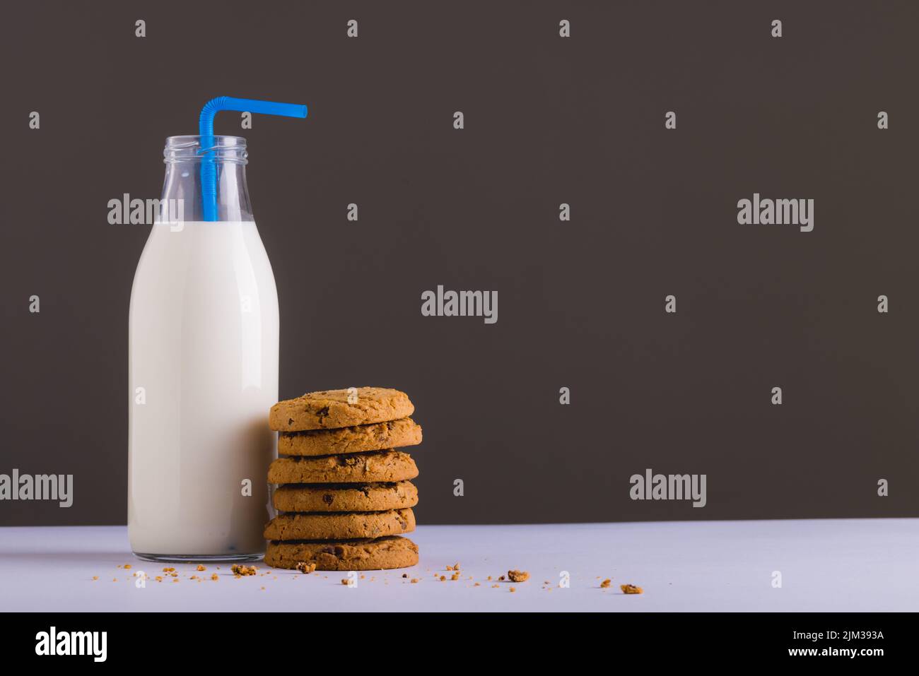 Milk bottle with straw by stack of cookies against gray background, copy space. unaltered, food, drink, studio shot and healthy food concept, Stock Photo