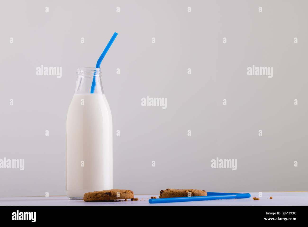 Milk bottle with straw by cookies against white background, copy space Stock Photo