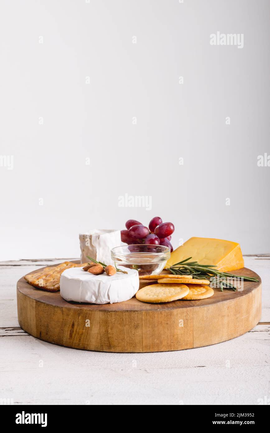 Cheese by grapes with herbs and crackers on wooden board against white background, copy space. unaltered, food, fruit and dairy product. Stock Photo