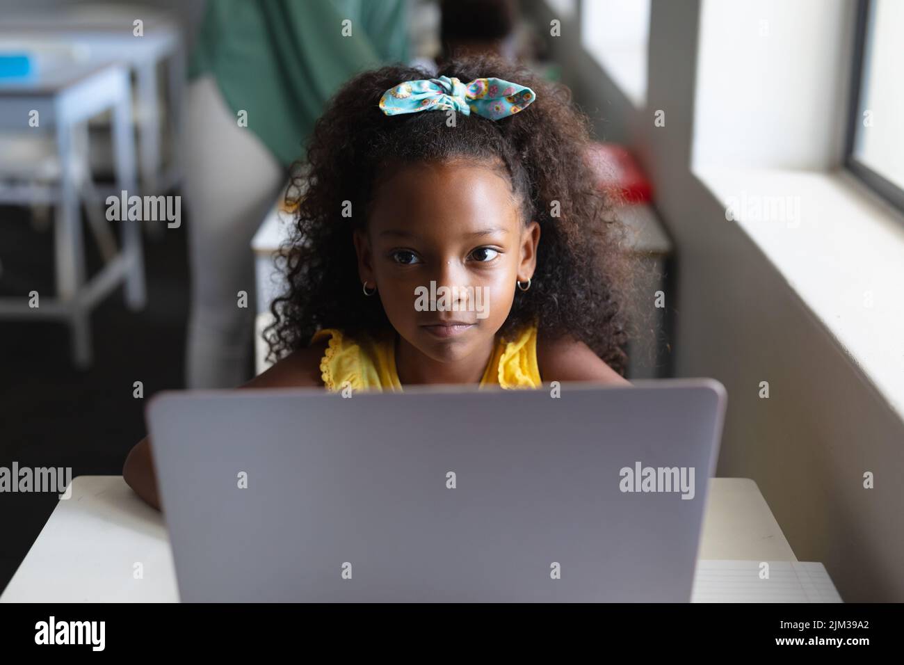 African american elementary schoolgirl looking away while sitting with laptop during computer class. unaltered, education, childhood, learning, wirele Stock Photo