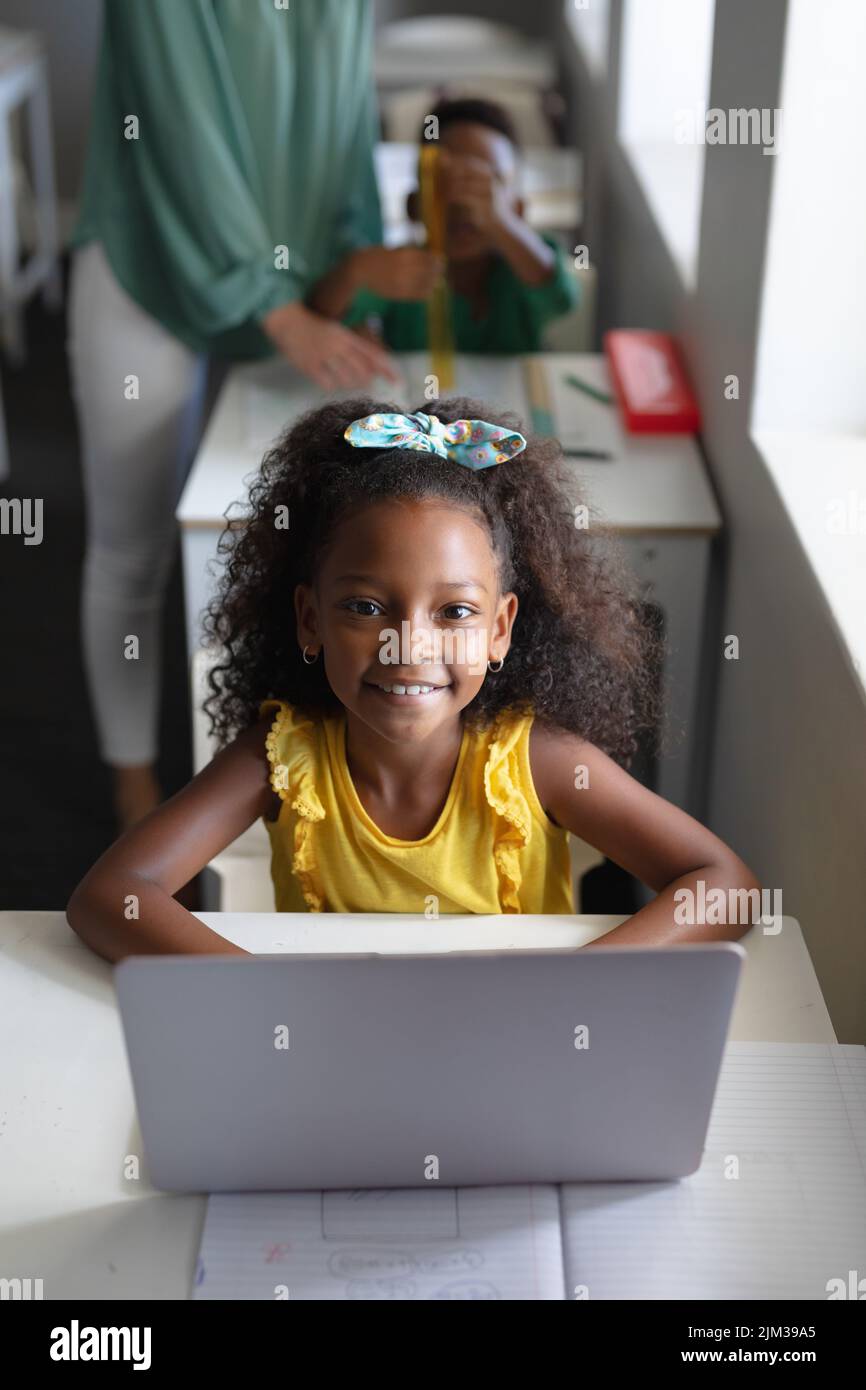 Portrait of smiling african american elementary schoolgirl using laptop at desk in classroom. unaltered, education, childhood, learning, wireless tech Stock Photo